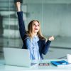 femme derrière son ordinateur qui est heureuse au travail, avec le poing levé